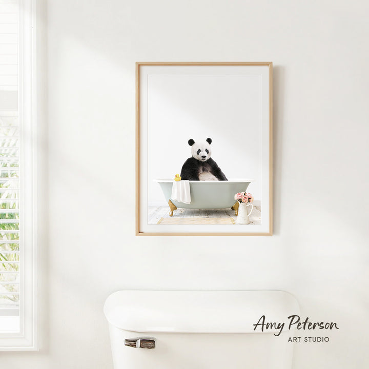 A framed image of a panda sitting in a bathtub, with a vase of flowers and a white toilet in the foreground.