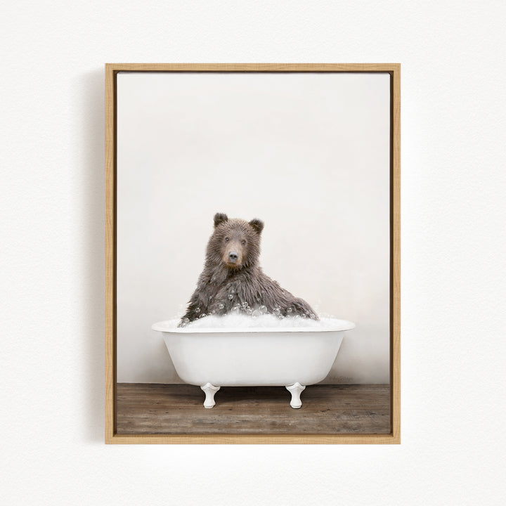 A brown bear sitting in a white bathtub filled with bubbles, looking directly at the camera.