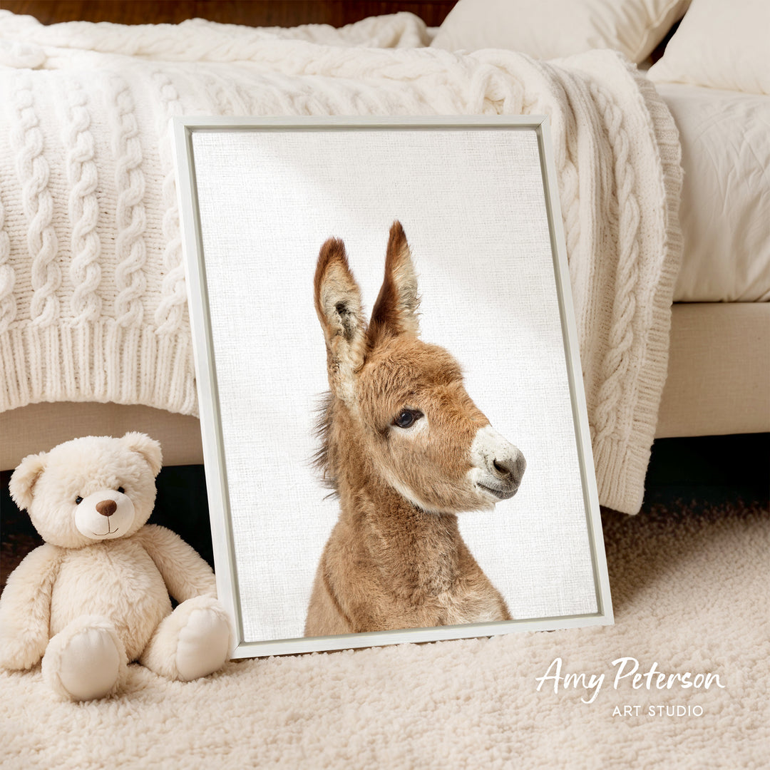 A framed image of a donkey is displayed on a bed, accompanied by a teddy bear and a blanket.