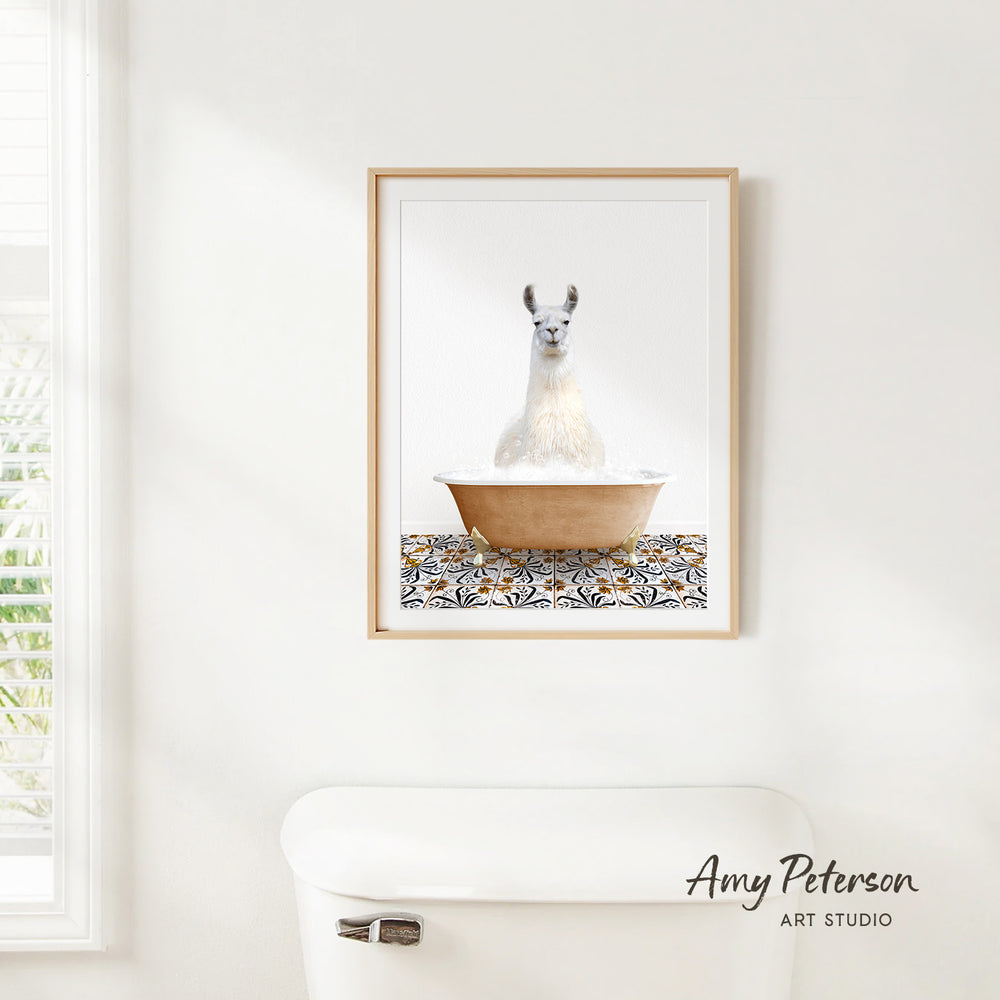 A framed image of a white llama sitting in a bathtub is hanging on a white wall above a white toilet.