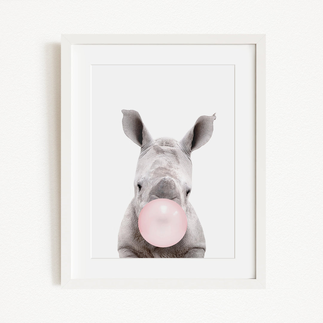 A white rhinoceros with its head tilted slightly to the left, blowing a pink bubble with its mouth.