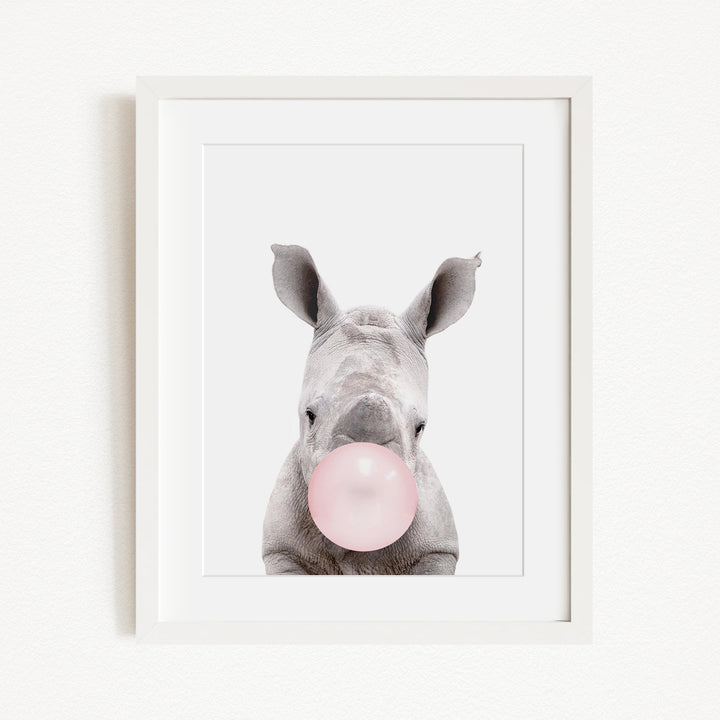 A white rhinoceros with its head tilted slightly to the left, blowing a pink bubble with its mouth.