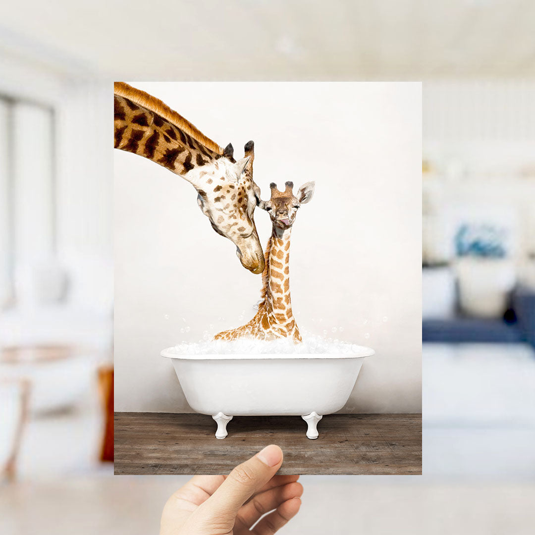 A mother giraffe and her baby giraffe are sitting together in a white bathtub, with the mother gently licking her baby.