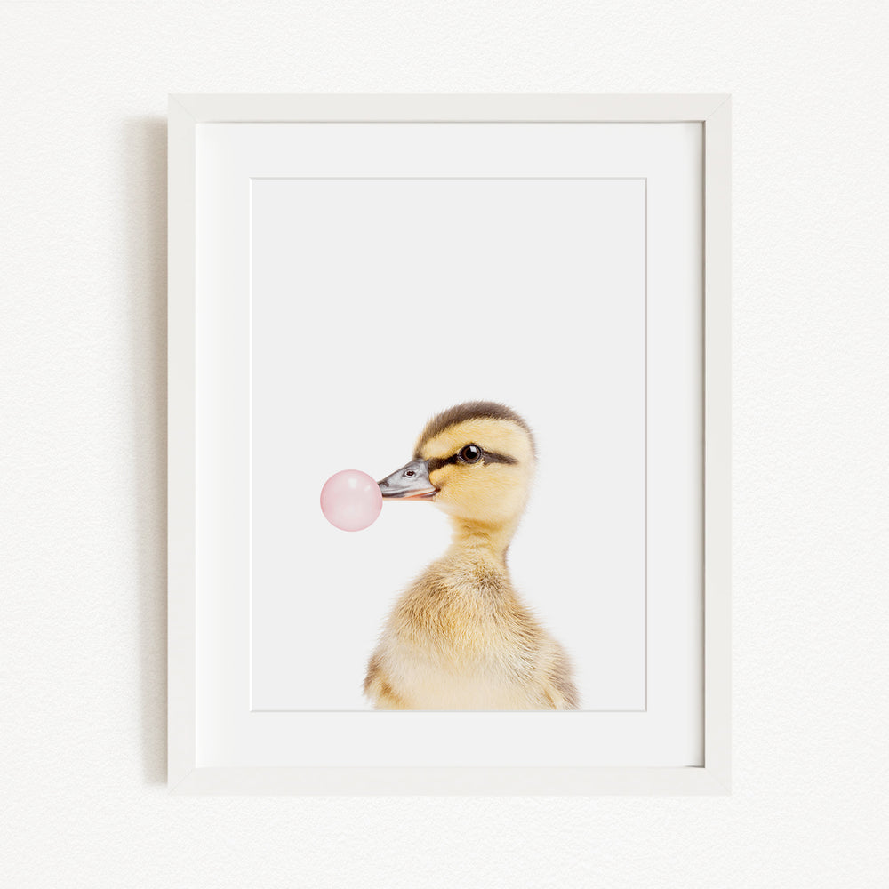 A cute baby duck blowing a bubble with a pink bubble gum bubble wand.