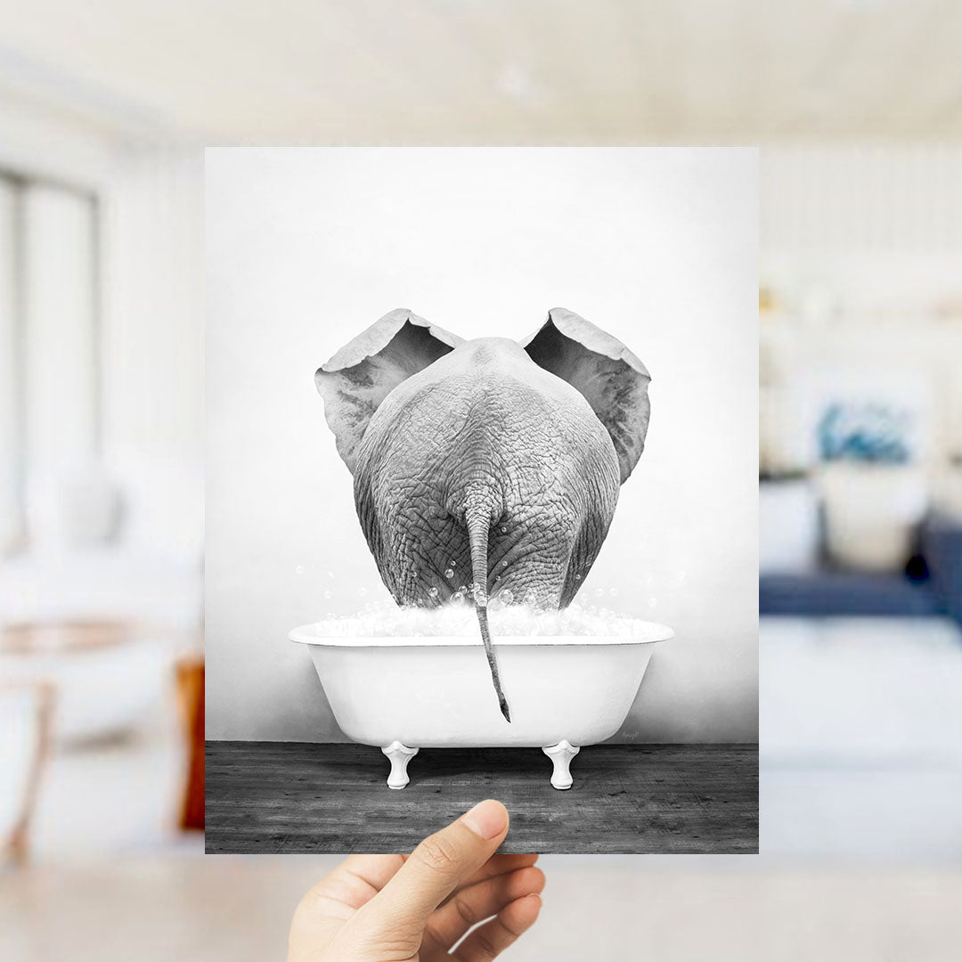 A hand holds up a black and white photograph of an elephant standing in a bathtub filled with water, creating a whimsical and playful scene.