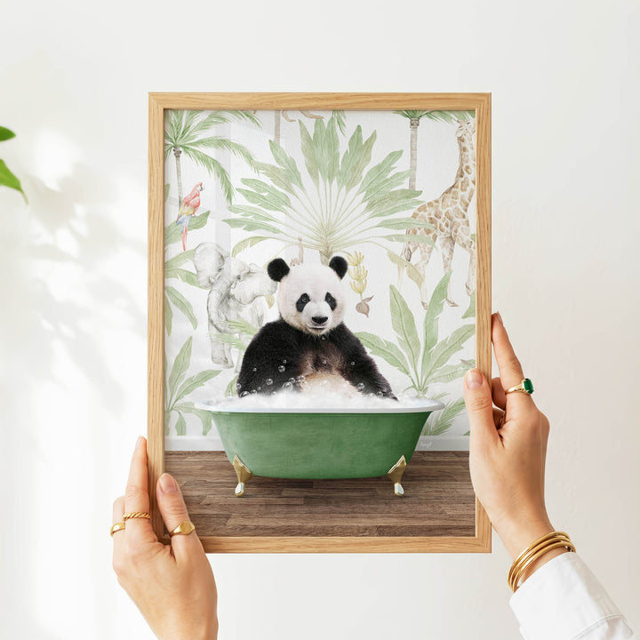 A person's hands are holding a framed picture of a panda sitting in a green bathtub, surrounded by tropical foliage.