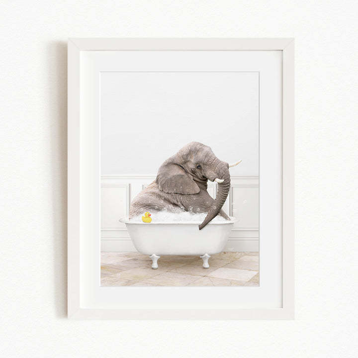 A gray elephant is sitting in a white bathtub, with a yellow rubber duck nearby.