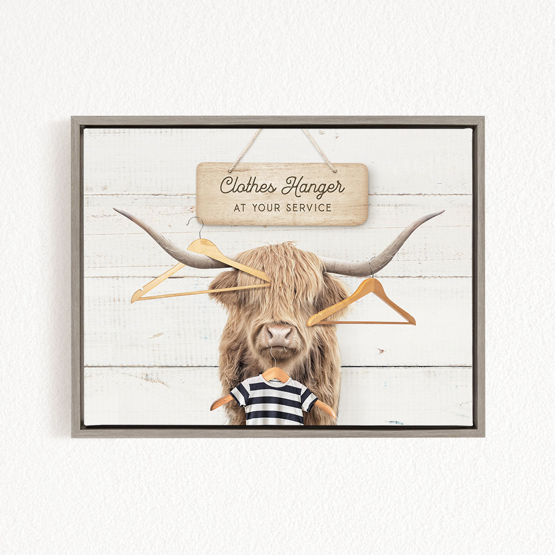 A wooden sign with the text "Clothes Hanger at your service" hangs above a large horned animal, which appears to be a yak or a yak-like creature.