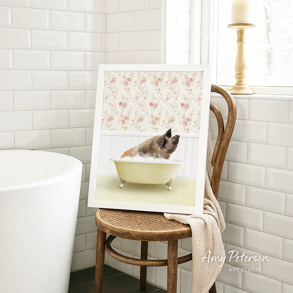 A framed image of a dog sitting in a bathtub, surrounded by a floral pattern, is displayed on a wooden chair in a bathroom setting.