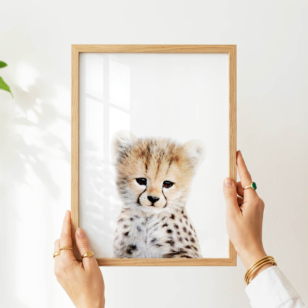 A person's hands are holding a wooden frame with a picture of a young cheetah inside it.