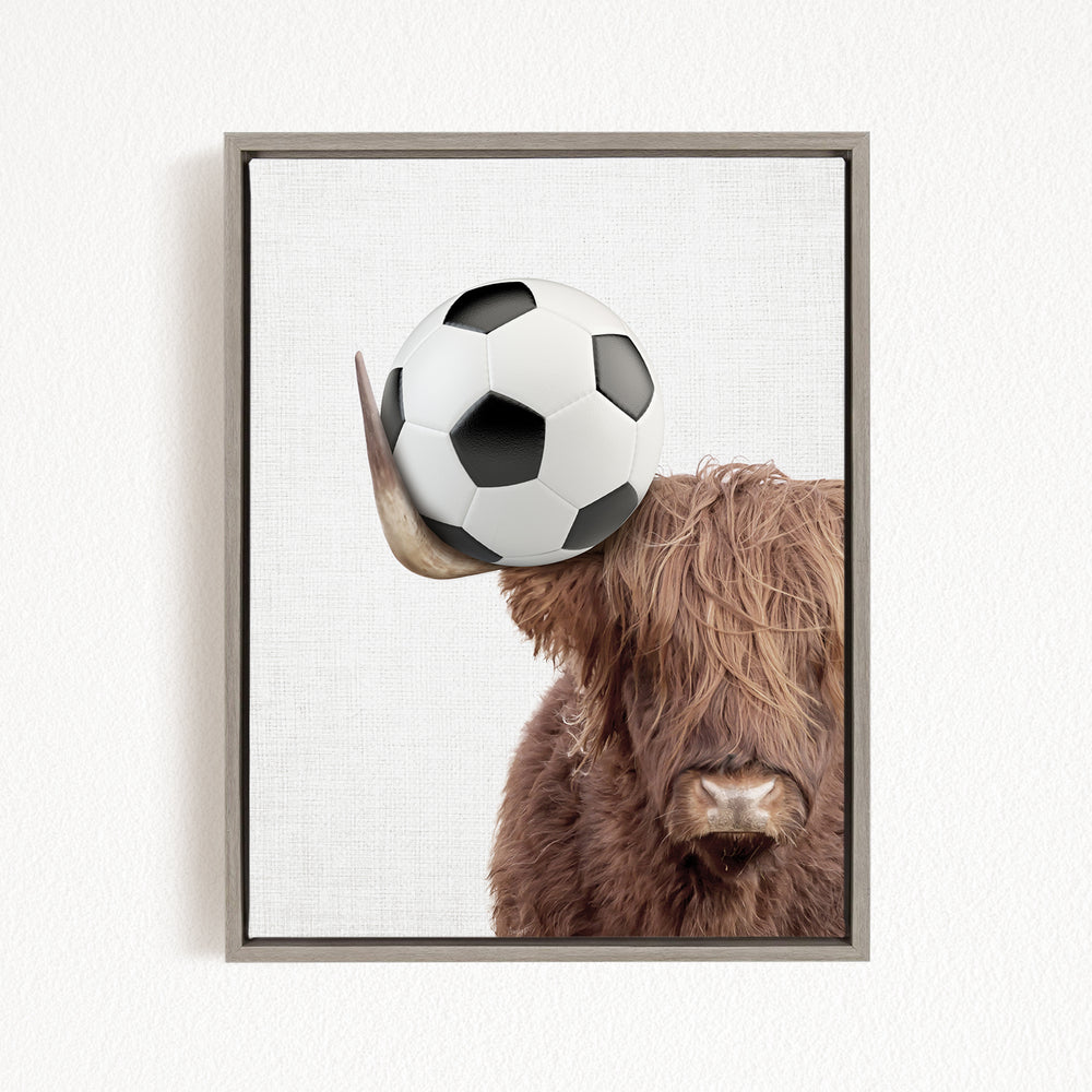 A framed image of a Highland cow balancing a soccer ball on its head.