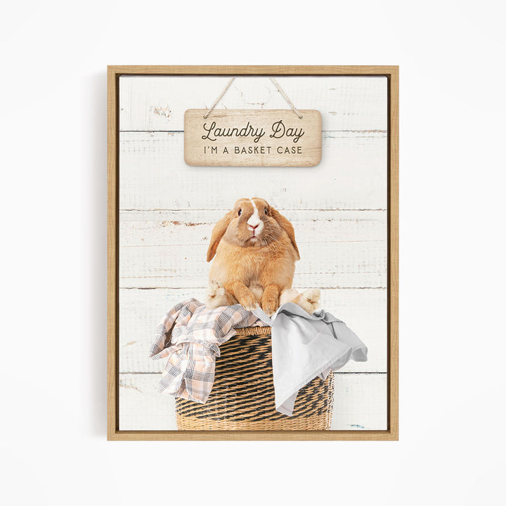 A wooden sign with the text "Laundry Day I'm a basket case" hangs above a woven basket containing a plaid shirt and a gray garment.