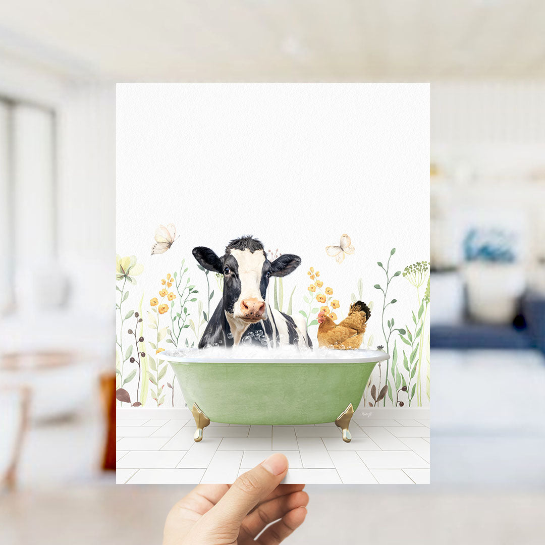 A hand holds up a framed image depicting a cow sitting in a bathtub filled with bubbles, surrounded by flowers and butterflies.