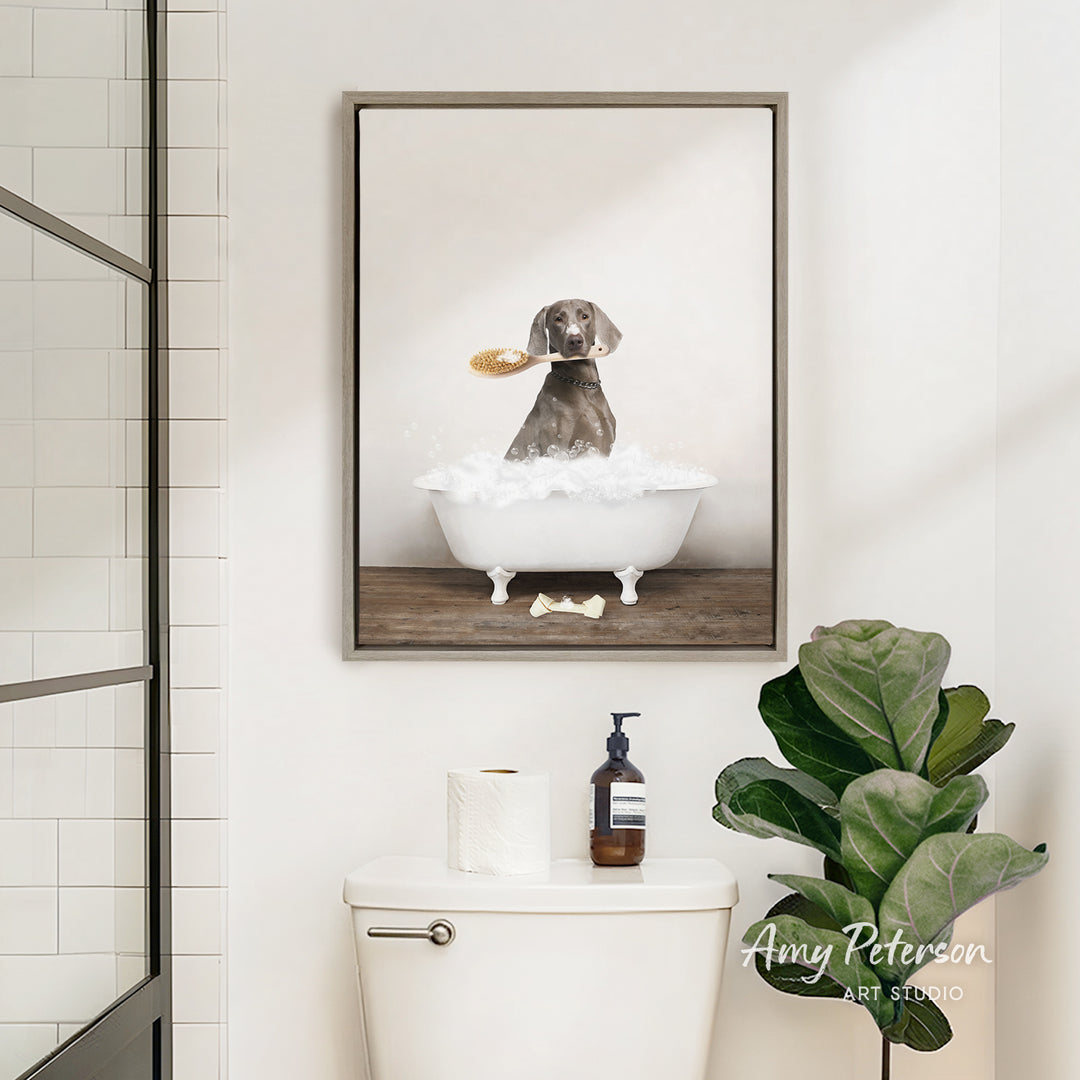 A framed image of a dog sitting in a bathtub, surrounded by bubbles, is displayed on the wall above a white toilet in a bathroom.
