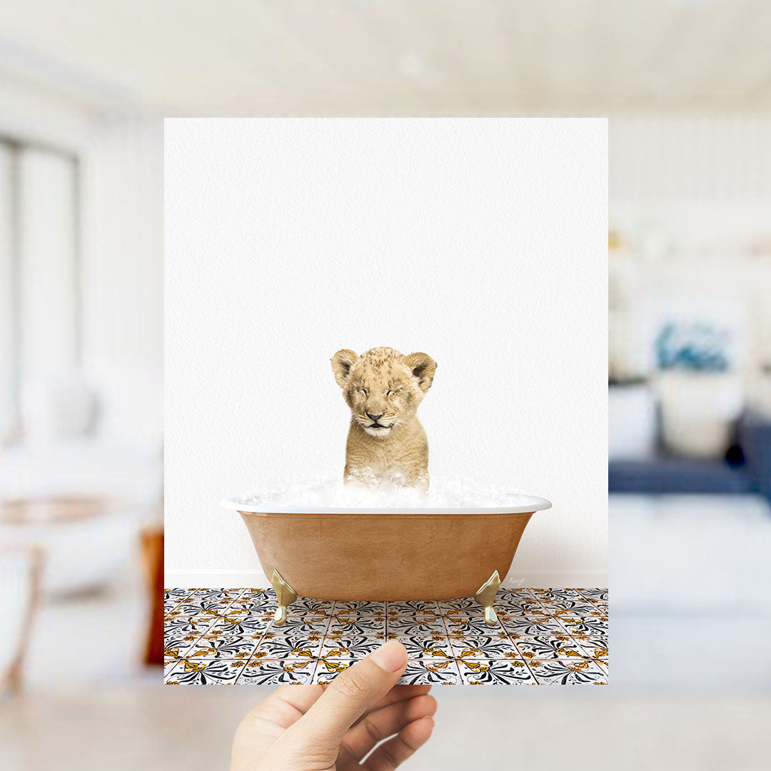 A hand holds up a framed image of a young lion cub sitting in a bathtub filled with water, surrounded by a patterned tile floor.