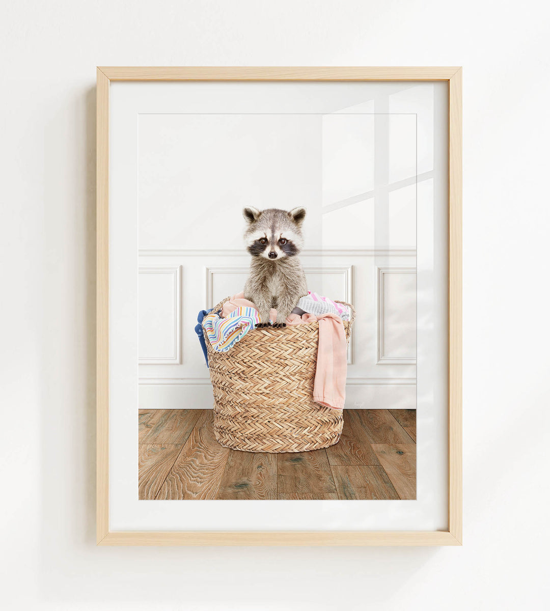 A raccoon sitting in a woven basket filled with clothes on a wooden floor.