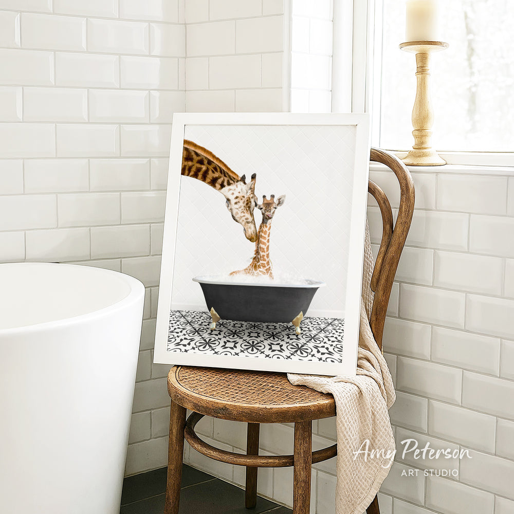 A framed image of a giraffe and a baby giraffe sitting in a bathtub, with a towel draped over the back of a wooden chair in a bathroom setting.