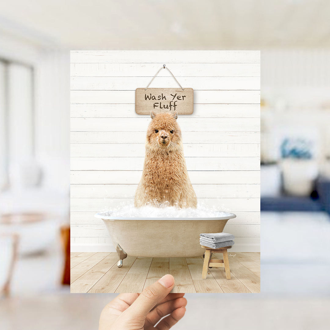 A hand holds up a framed image of a fluffy brown dog sitting in a bathtub filled with bubbles, with a sign above that says "Wash Your Fluff".