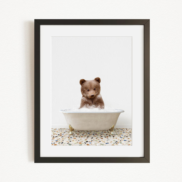 A cute brown bear cub sitting in a white bathtub filled with bubbles, surrounded by a mosaic floor.