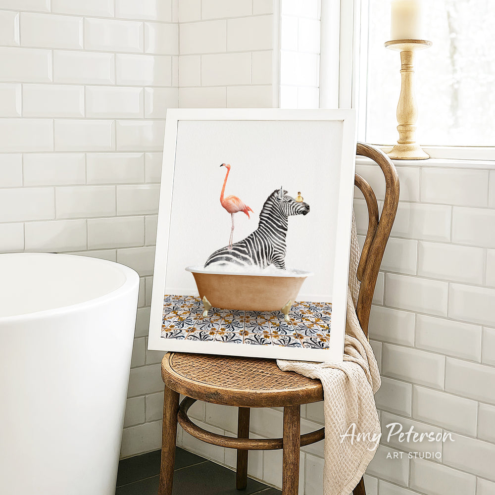 A framed image of a zebra sitting in a bathtub, with a pink flamingo standing on its back, is displayed on a wooden chair in a bathroom setting.
