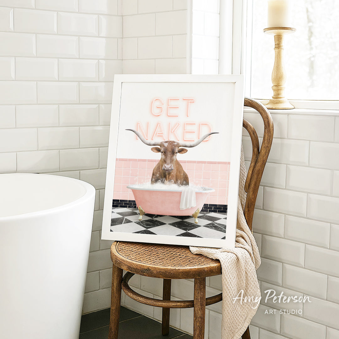 a framed artwork depicting a bull with horns sitting in a pink bathtub, surrounded by pink and black tiles, with the text "GET NAKED" displayed prominently.