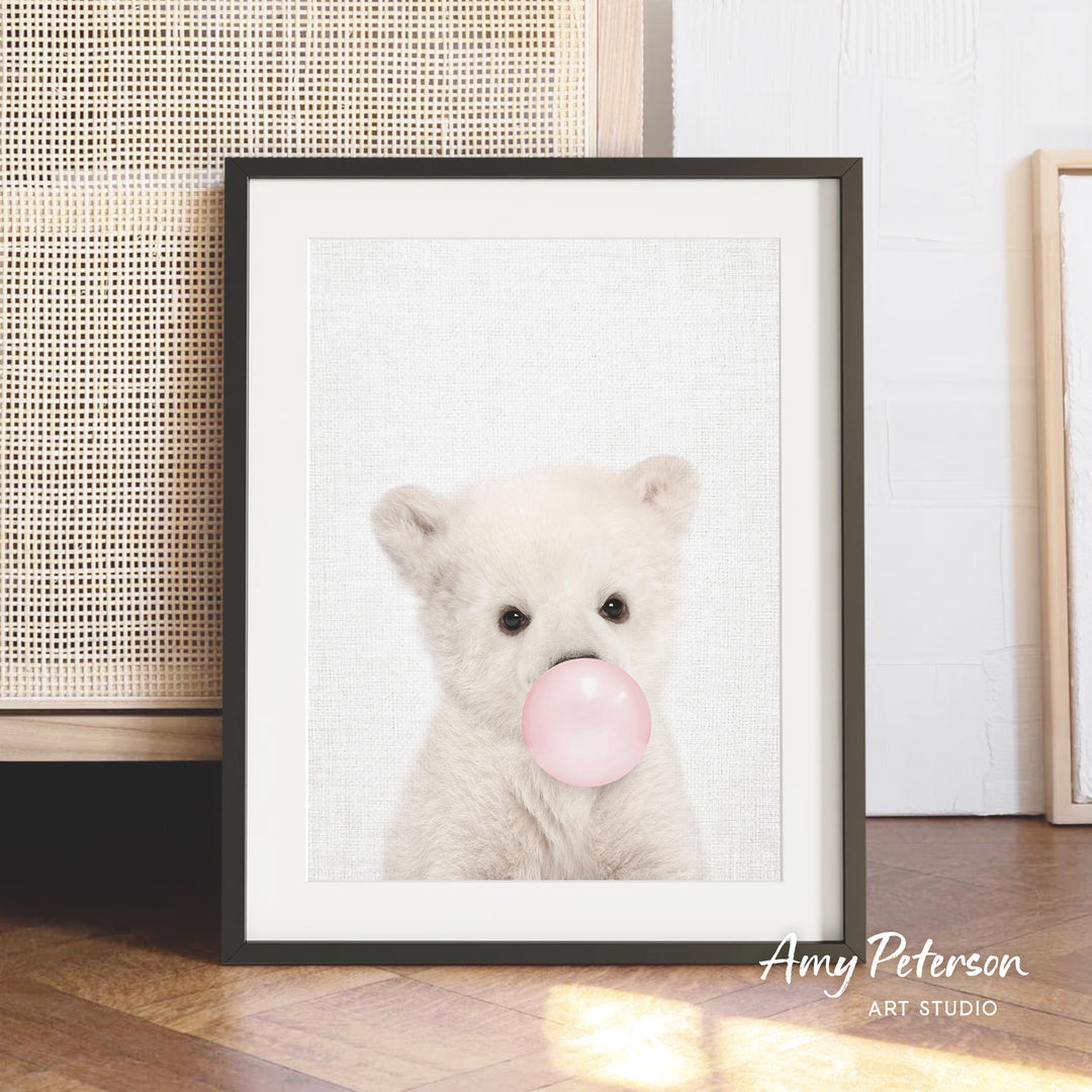 A framed photograph of a cute white bear blowing a bubble with a pink bubblegum bubble.