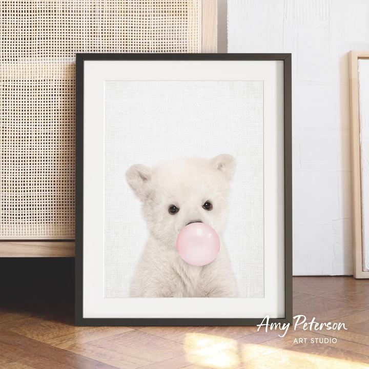 A framed photograph of a cute white bear blowing a bubble with a pink bubblegum bubble.
