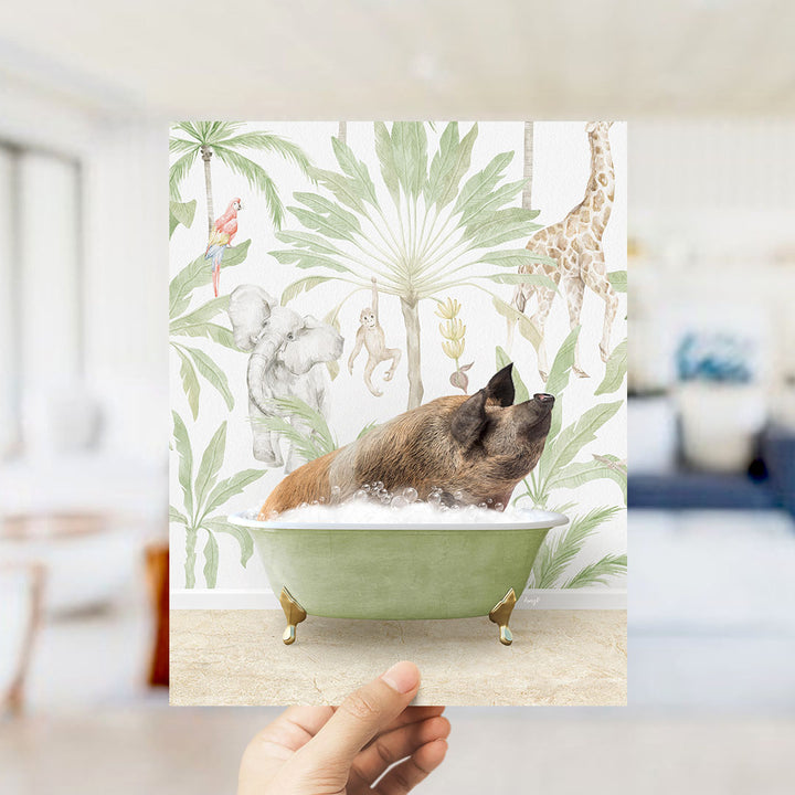 A hand holds up a framed print featuring a whimsical illustration of a pig relaxing in a bathtub surrounded by tropical foliage, including a giraffe and other animals.