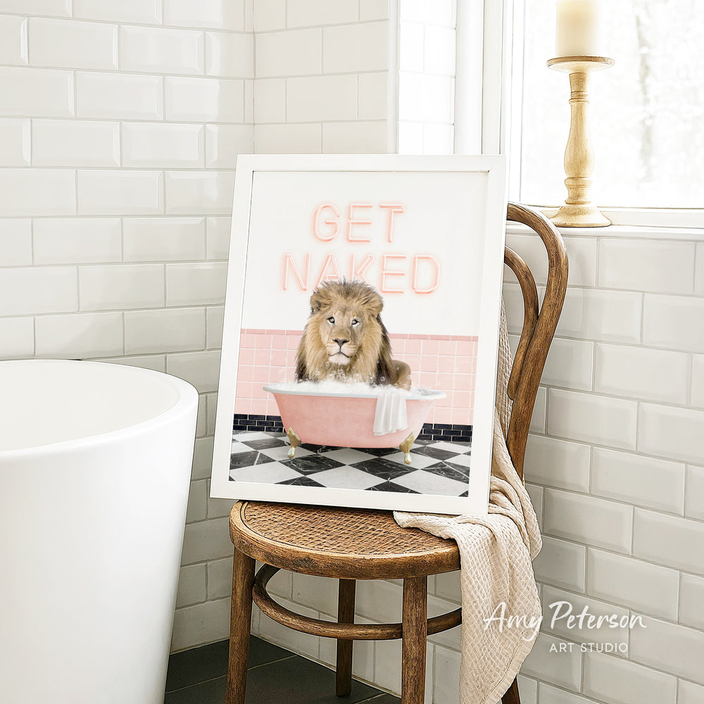 A framed image of a lion sitting in a pink bathtub with the text "GET NAUGED" on it, placed on a wooden chair in a bathroom setting.