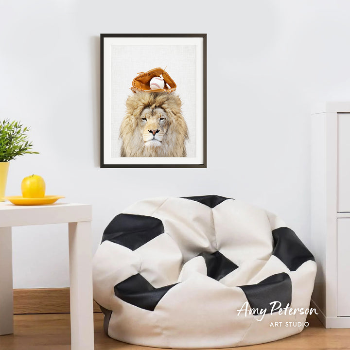 a framed picture of a lion wearing a baseball cap and a baseball glove, hanging on a white wall above a black and white bean bag chair.
