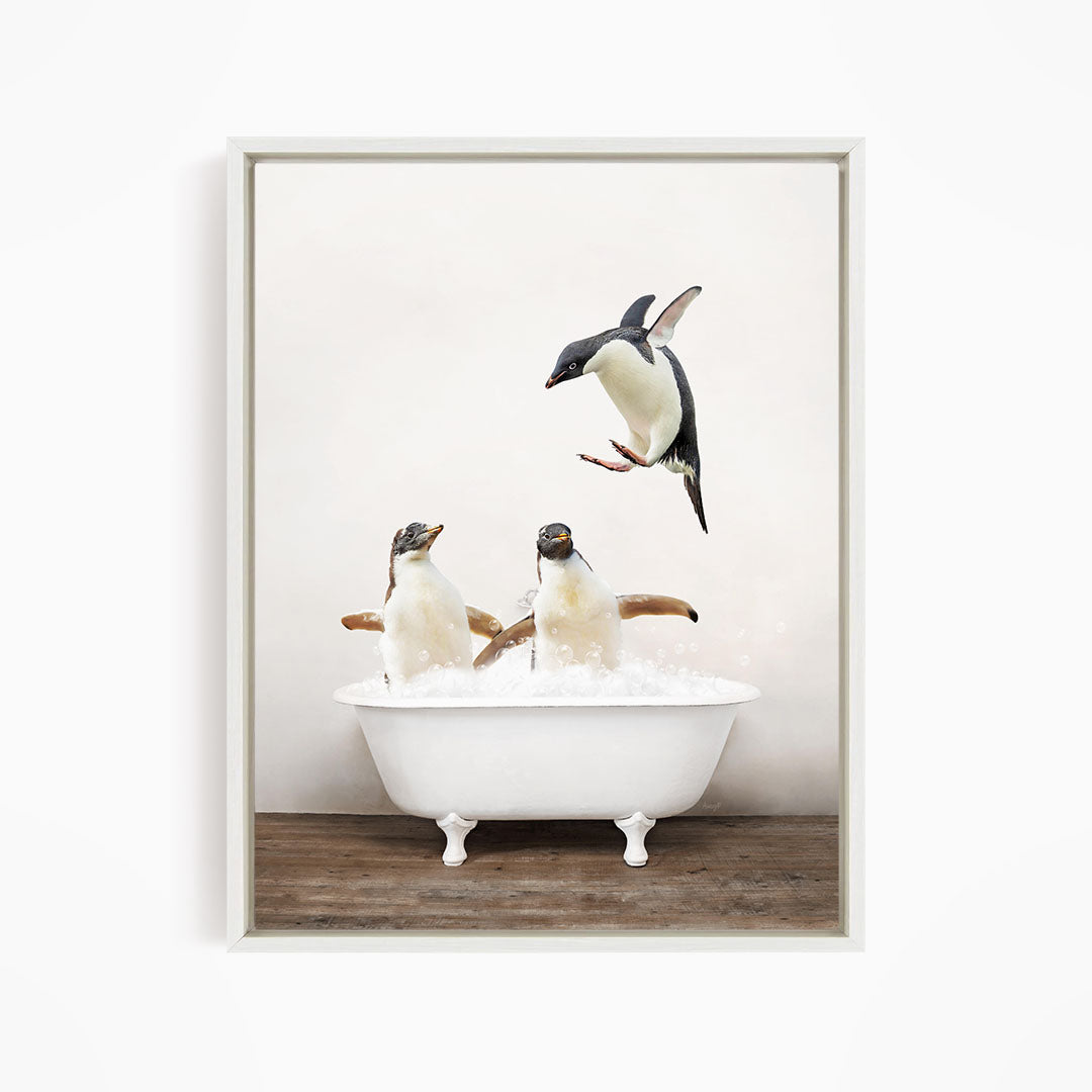 A framed image depicting three penguins sitting in a white bathtub, with one penguin flying towards the tub.