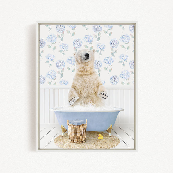 A polar bear is sitting in a blue bathtub filled with water, surrounded by a wicker basket, rubber duckies, and a floral patterned wall behind it.