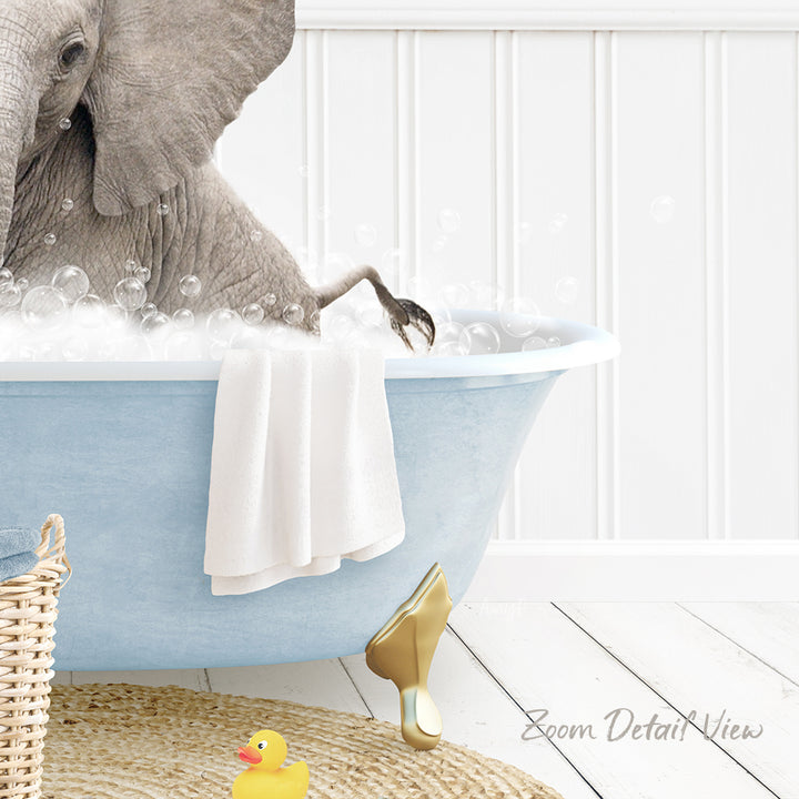 A gray elephant is sitting in a blue bathtub filled with bubbles, surrounded by a yellow rubber duck and a white towel.