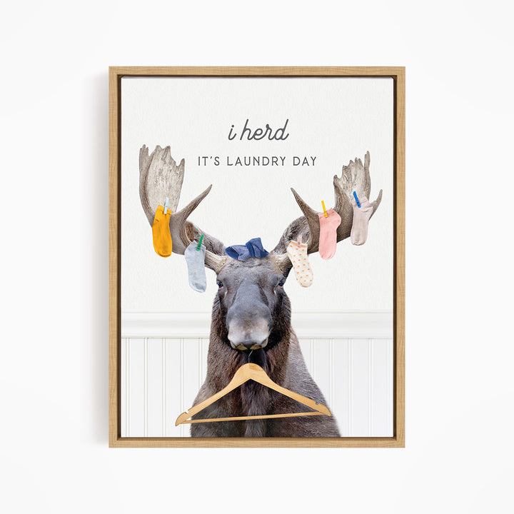 A framed image depicting a moose with a laundry basket, displaying socks hanging from its antlers.