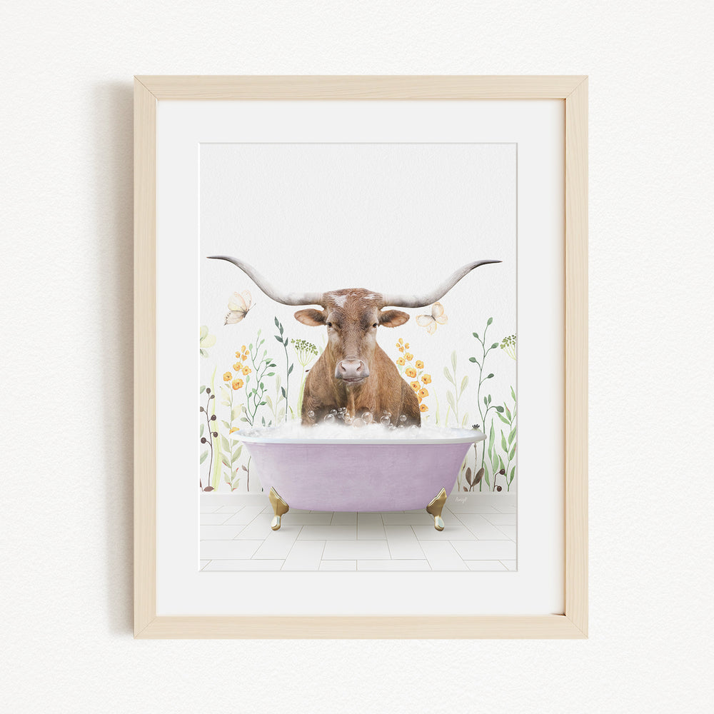 A framed print depicting a brown cow with large horns sitting in a purple bathtub filled with water, surrounded by flowers and plants.