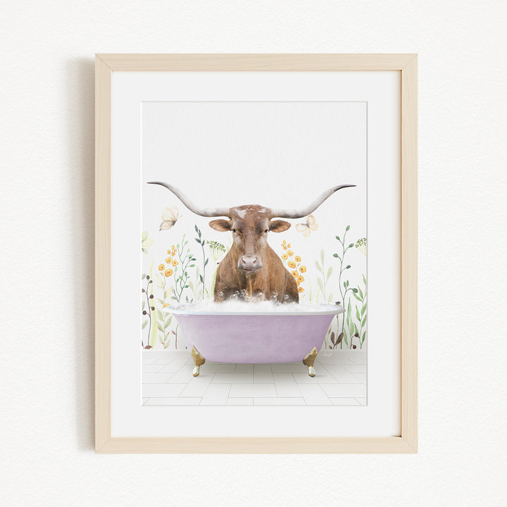 A framed print depicting a brown cow with large horns sitting in a purple bathtub filled with water, surrounded by flowers and plants.