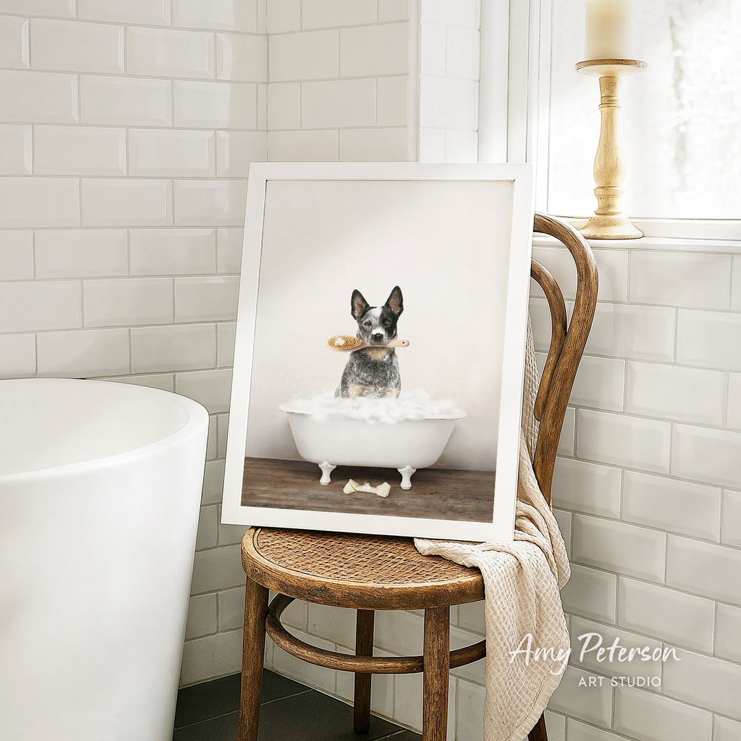 A framed photograph of a dog sitting in a bathtub, holding a toy, is displayed on a wooden chair in a bathroom setting.