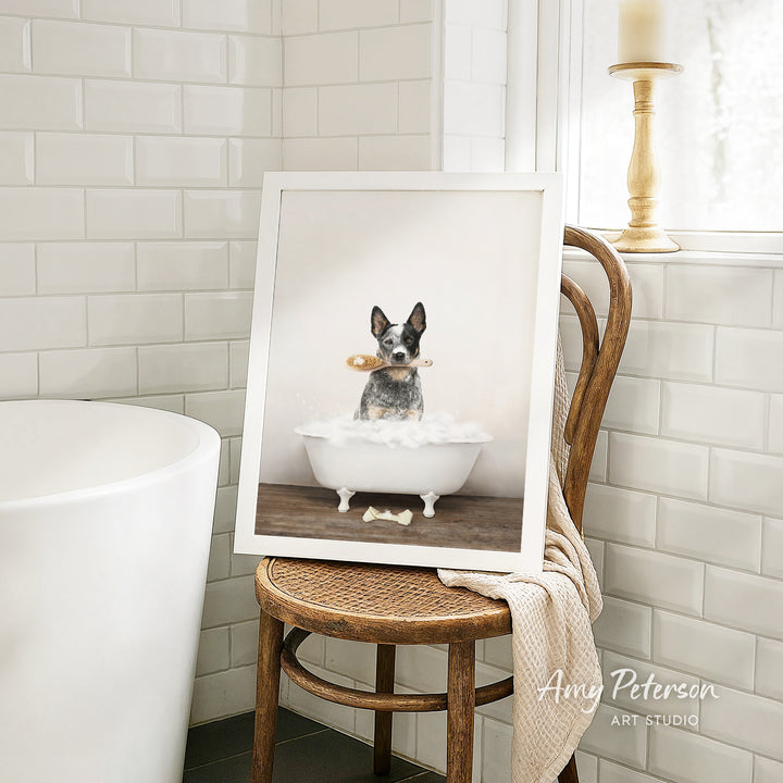 A framed photograph of a dog sitting in a bathtub, holding a toy, is displayed on a wooden chair in a bathroom setting.