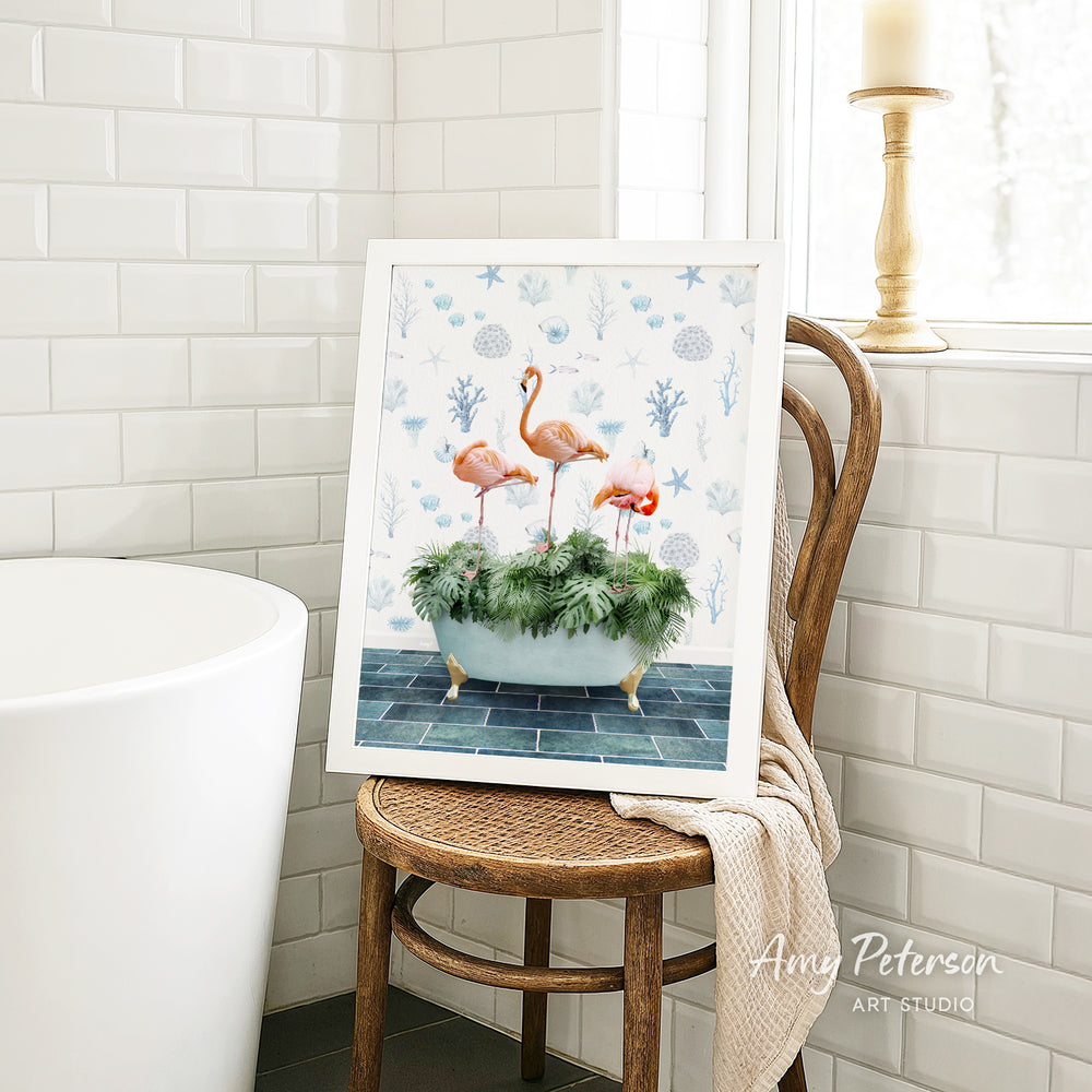 A framed painting of three flamingos in a bathtub is displayed on a wooden chair in a bathroom setting.