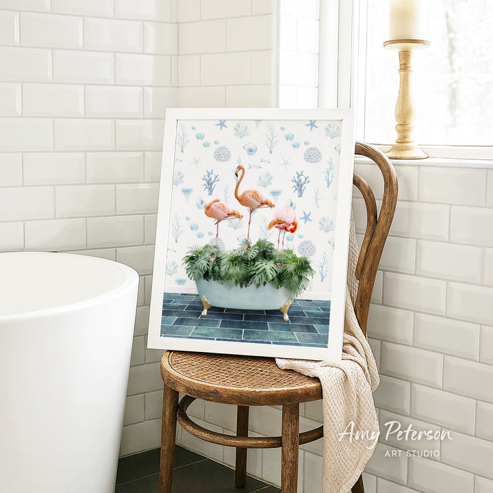 A framed painting of three flamingos in a bathtub is displayed on a wooden chair in a bathroom setting.