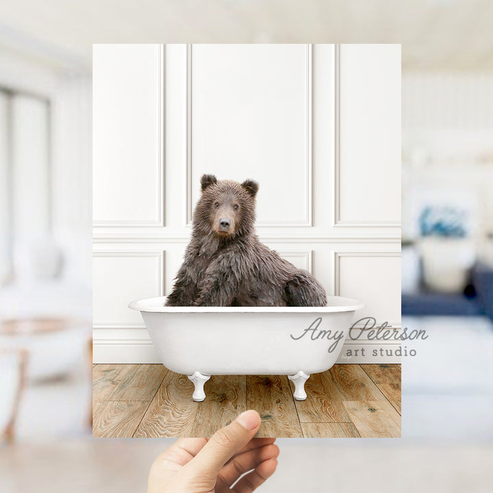 a hand holding a photo of a bear in a bathtub