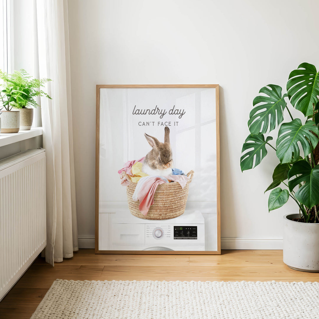 A framed poster with a rabbit sitting in a basket of laundry, accompanied by the text "laundry day can't face it".