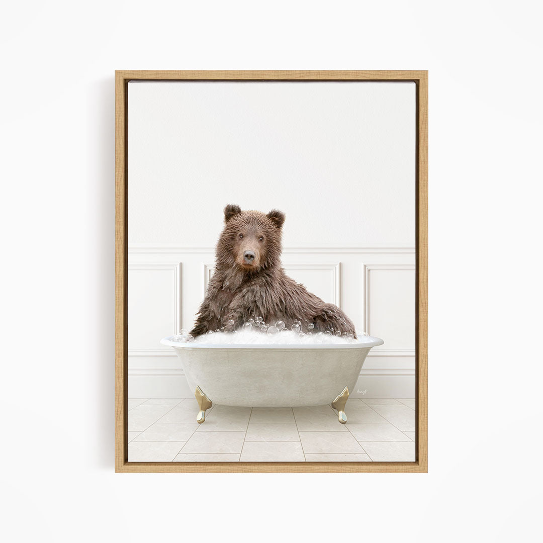 A brown bear sitting in a white bathtub filled with bubbles, looking directly at the camera.