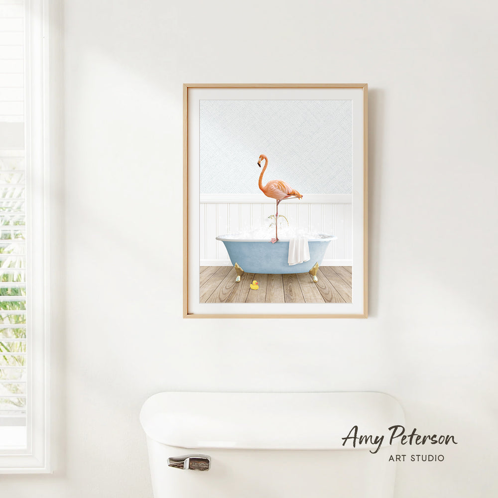 A framed print of a flamingo standing in a bathtub is hanging on a white wall in a bathroom.