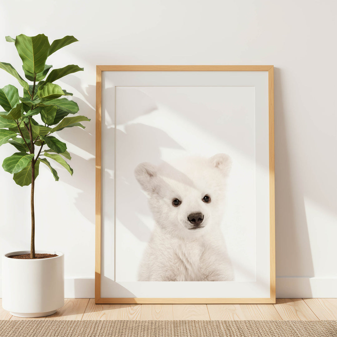 a white polar bear in a framed picture, placed on a wooden floor next to a potted plant.