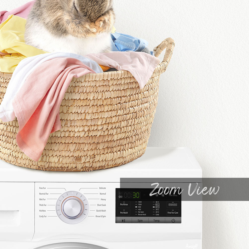 A cat sitting in a woven laundry basket filled with clothes, with a white washing machine in the background displaying a "Zoom View" interface.