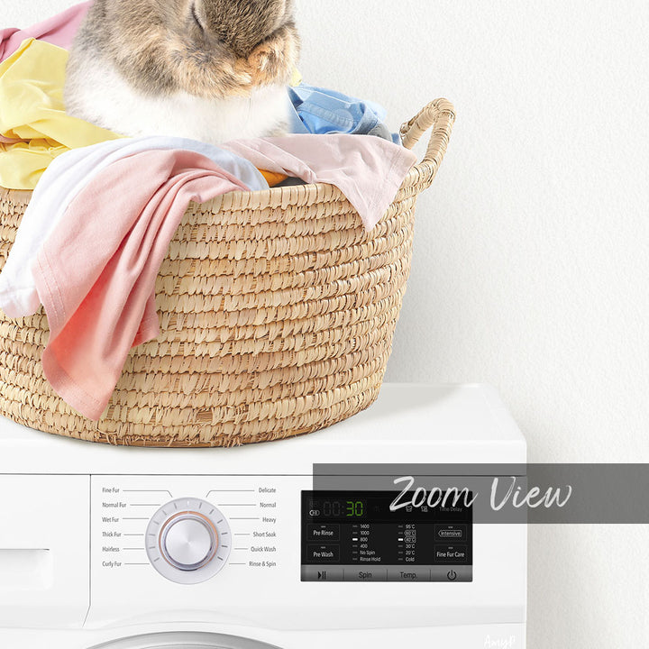 A cat sitting in a woven laundry basket filled with clothes, with a white washing machine in the background displaying a "Zoom View" interface.