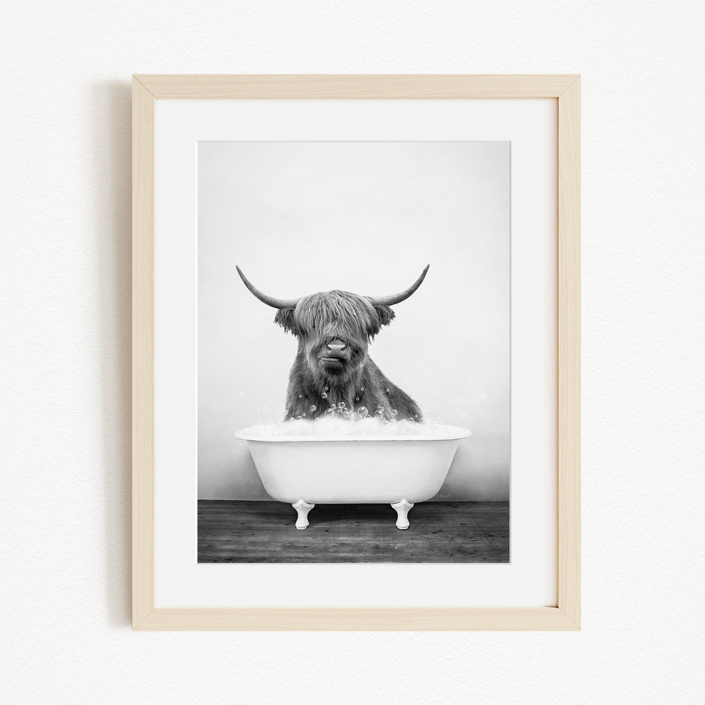 A black and white photograph of a Highland cow sitting in a bathtub filled with water.