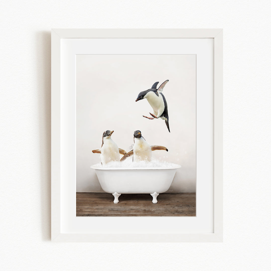 A framed image depicting two penguins sitting in a white bathtub, with one penguin flying towards the other.