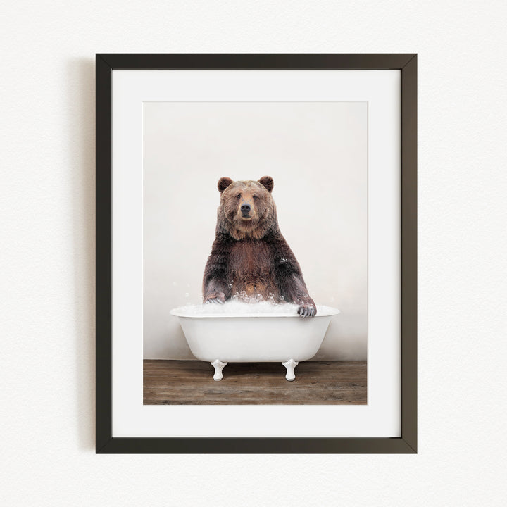 A brown bear sitting in a white bathtub filled with water, appearing to enjoy the bath.
